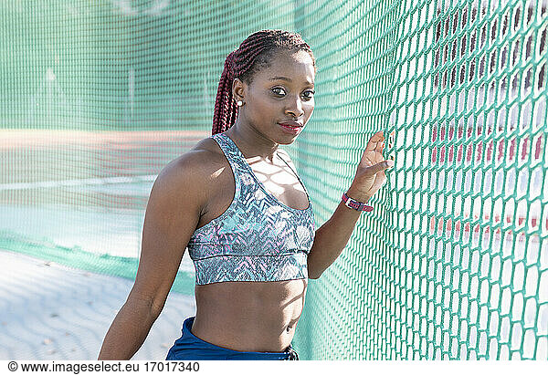 Female sportsperson with braided hair standing by green net in sunlight