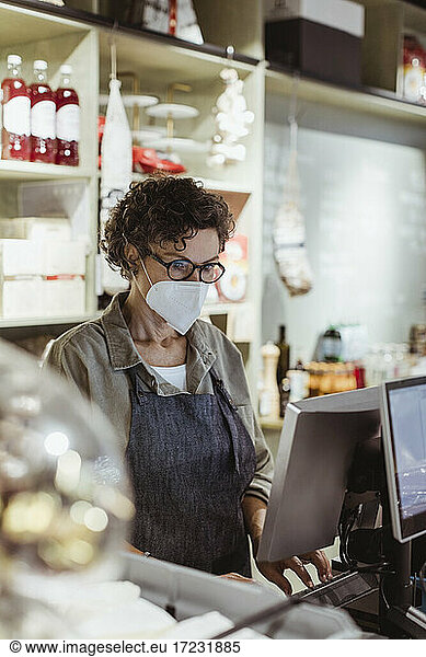 Female store owner working on computer in deli store during pandemic