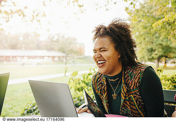 Female student laughing while studying online through laptop in college campus