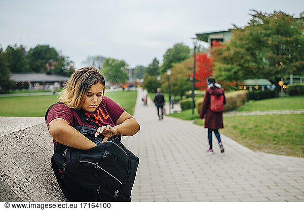 Female student peeking in backpack while standing in college campus