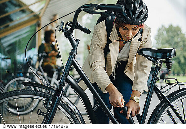 Female student unlocking bicycle at parking station in college campus