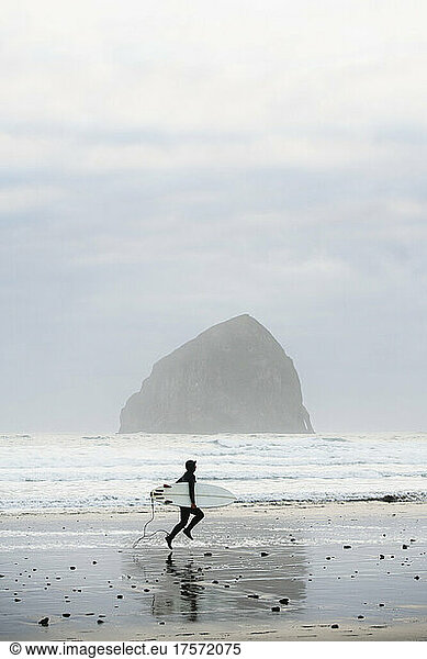 Female surfer running to catch waves is Coastal Oregon