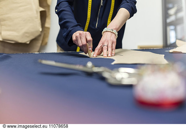 Female tailor marking fabric with pattern in menswear workshop