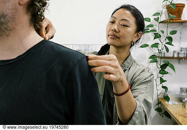 Female tailor measuring shoulder of male customer at workshop