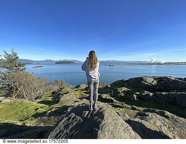 Female taking photo on a cliff with water views