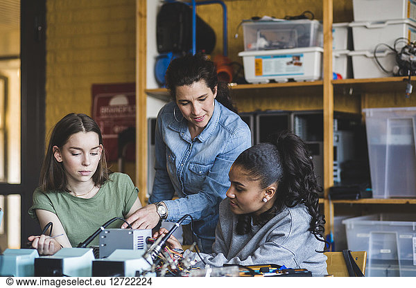 Female teacher assisting high school teenage students preparing robot on desk in classroom