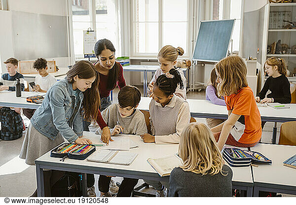 Female teacher assisting students learning together in classroom