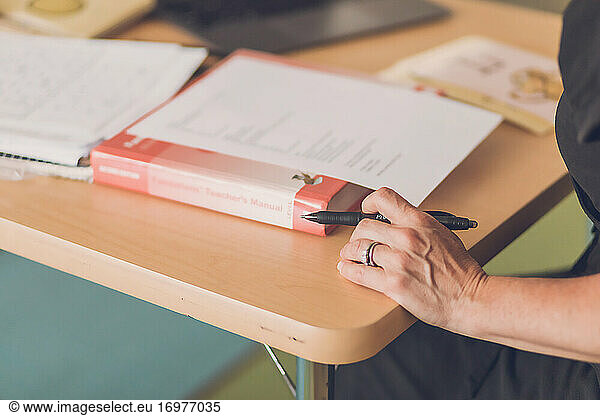 Female teacher organizing notes on desk  focus on hand and black pen.