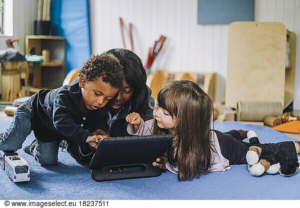 Female teacher sharing digital tablet with children in child care center