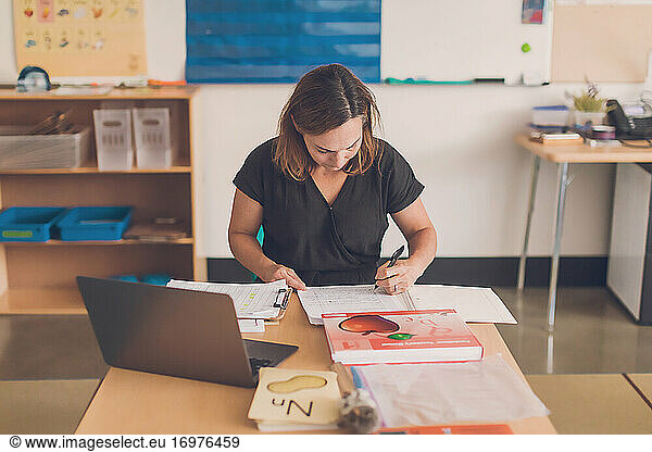 Female teacher writing down on her notebook in her classroom.