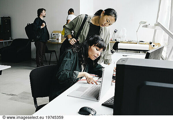 Female technician repairing laptop while sitting near customer at store