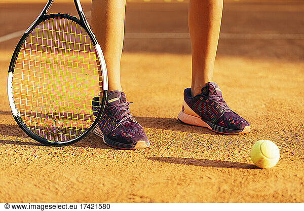 Female tennis player with racket and ball standing at sports court