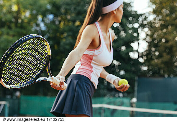 Female tennis player with racket serving ball at sports court