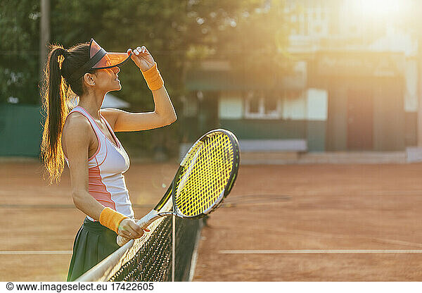 Female tennis player with racket standing by net at sports court