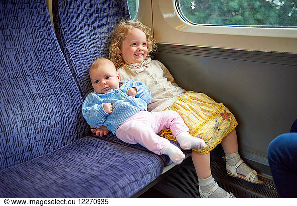 Female toddler sitting on train with baby sister