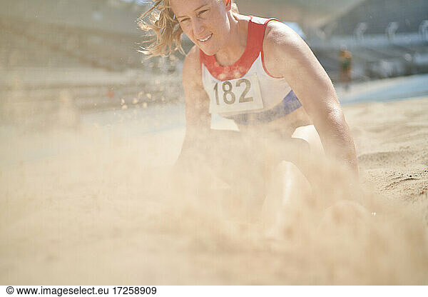 Female track and field athlete landing in long jump sand