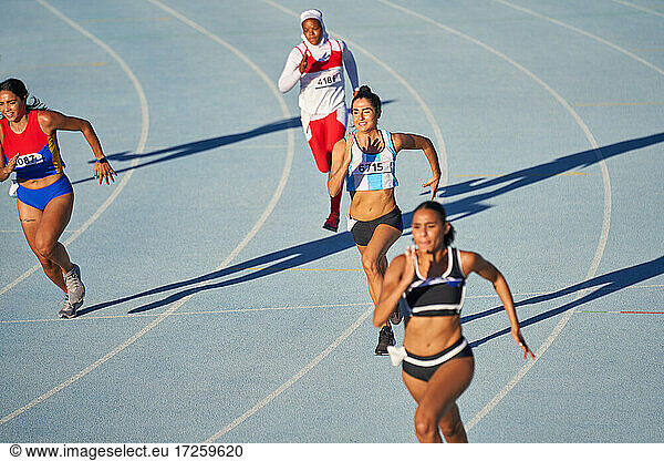 Female track and field athletes running on sunny blue track