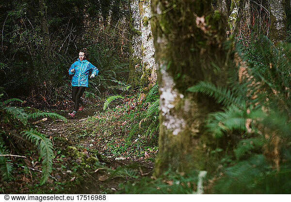 Female trail runner runs on rocky trail in forest surrounded by ferns