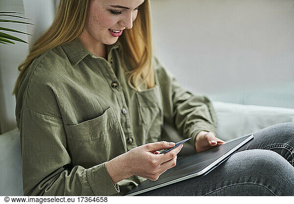 Female trainee sitting with credit card and digital tablet in office