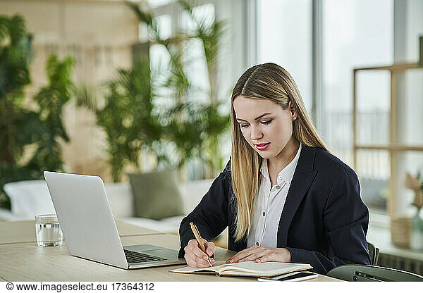 Female trainee writing in dairy while sitting at desk in office