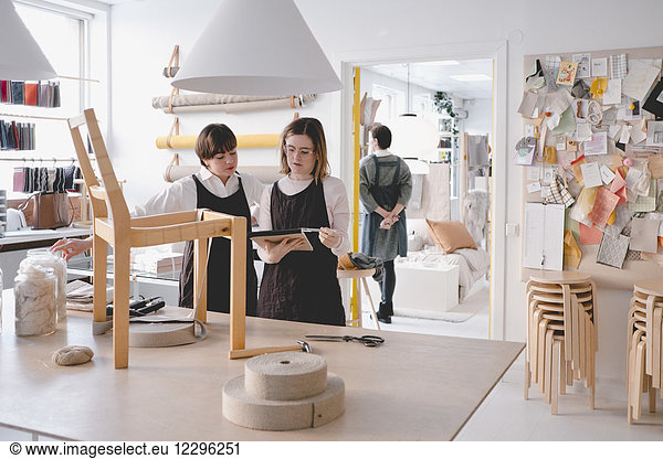 Female upholstery workers reading note pad with chair on desk in workshop