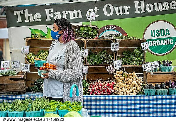 Female vendor wearing face mask holds cartons of vegetables  Silver Spring Farmers Market  Silver Spring  MD.