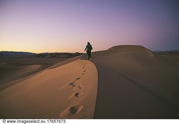 Female walking on a sand dune at sunset