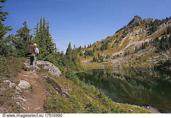 Female with backpack standing next to alpine lake in the cascades