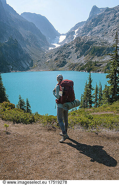 Female with backpack standing next to amazing blue colored alpine lake