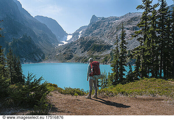 Female with backpack standing next to gorgeous alpine lake