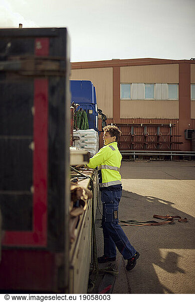 Female worker unloading goods from truck outside factory on sunny day