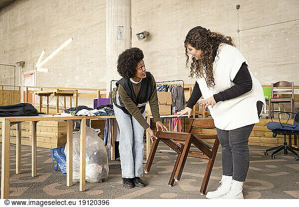 Female workers discussing over wooden chair at recycling center