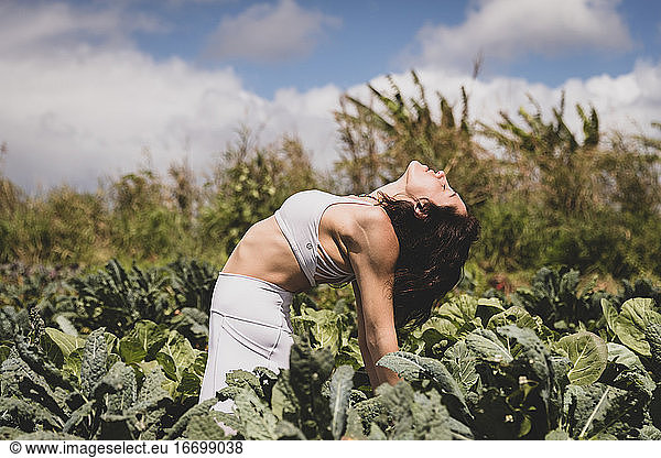 Female yogi backbends in field of vegetables