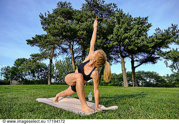 Female yogi doing a rotated triangle pose outside on sunny day in park