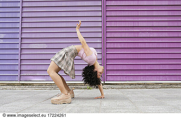 Female young dancer bending over backwards by colorful wall