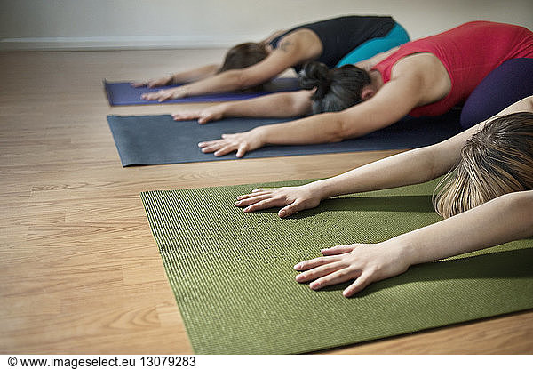 Females performing yoga in child's pose at health club
