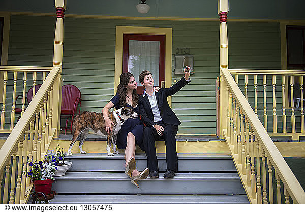 Females with dog taking selfie through mobile phone while sitting on steps at porch