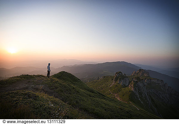 Fernansicht eines Wanderers  der bei Sonnenuntergang auf einem Berg vor klarem Himmel steht