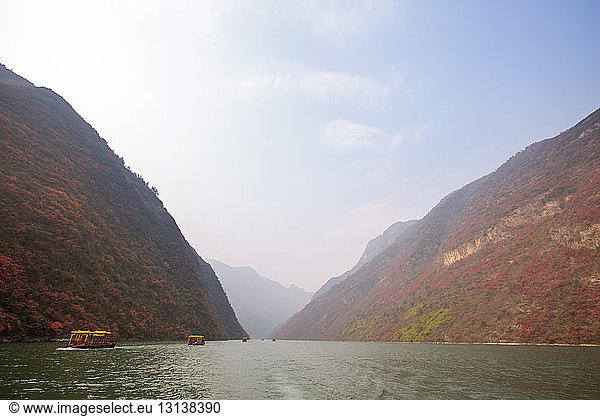 Ferry boats moving in river amidst mountains against sky