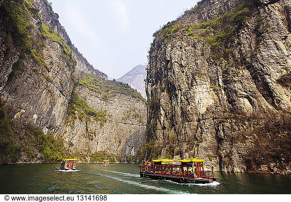 Ferry boats moving in Yangtze River amidst mountains against clear sky