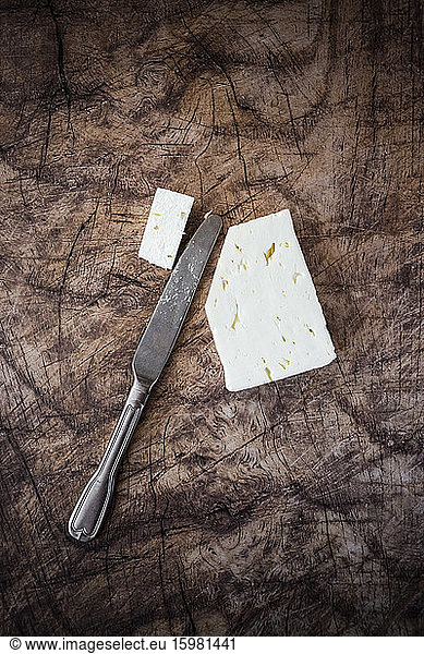 Feta cheese and table knife on wooden surface
