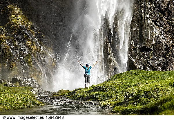 Figur stehend vor einer Wasserfall-Gischt  in grüner Naturlandschaft