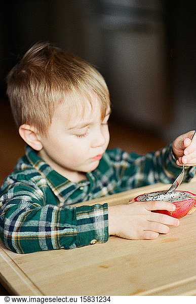 Film photo of a little boy eating a dragon fruit with a spoon.