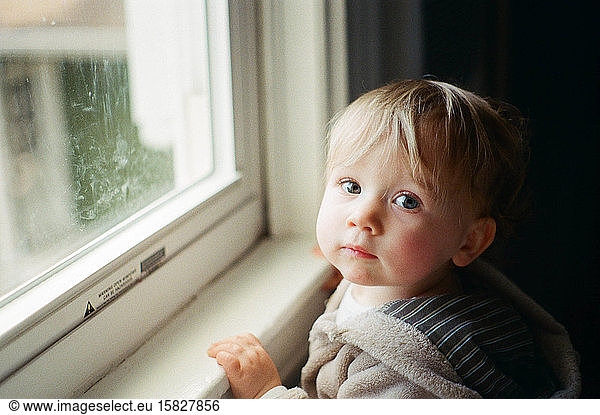 Film photo of a little girl standing by a window.