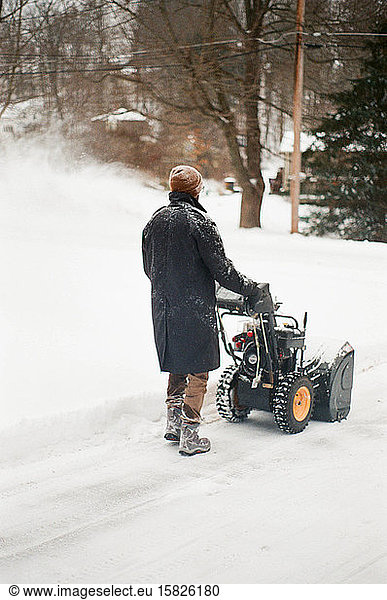 Film photo of a man snow blowing in his driveway.