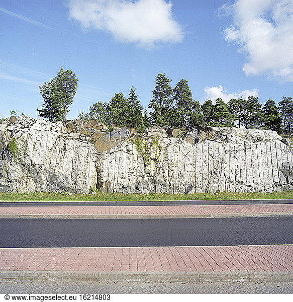 Finland  Rockface with trees  country road in the foreground