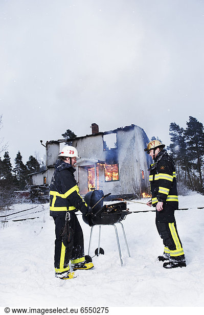 Firefighters having barbeque in front of burning house