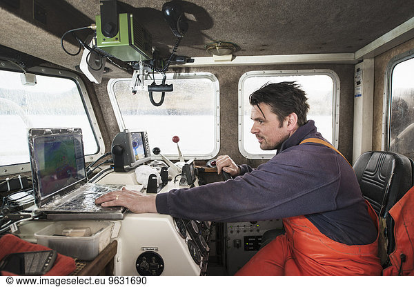 Fisherman driving fishing boat using laptop