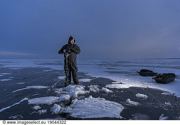 Fisherman holding ice drill on the frozen lake