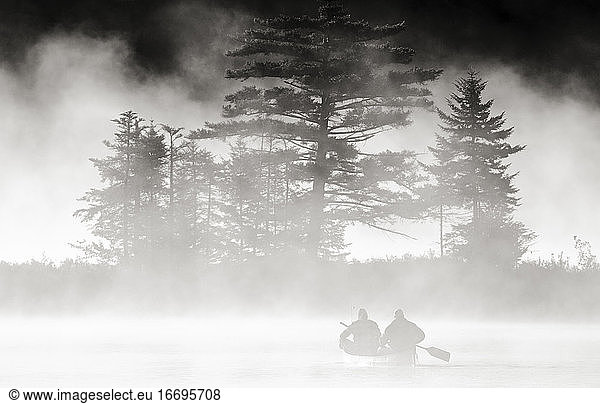 Fishermen canoe in fog to reach fishing spot on secluded Vermont Lake.